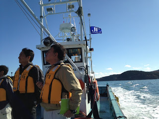 数名の人がライフジャケットを着て船に乗り、沖に向かって進んでいる様子の写真