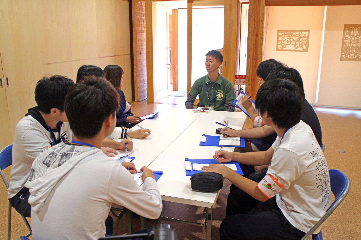 2台並べた長机を囲んで座った学生たちが、関係者の男性にインタビューを行っている様子の写真