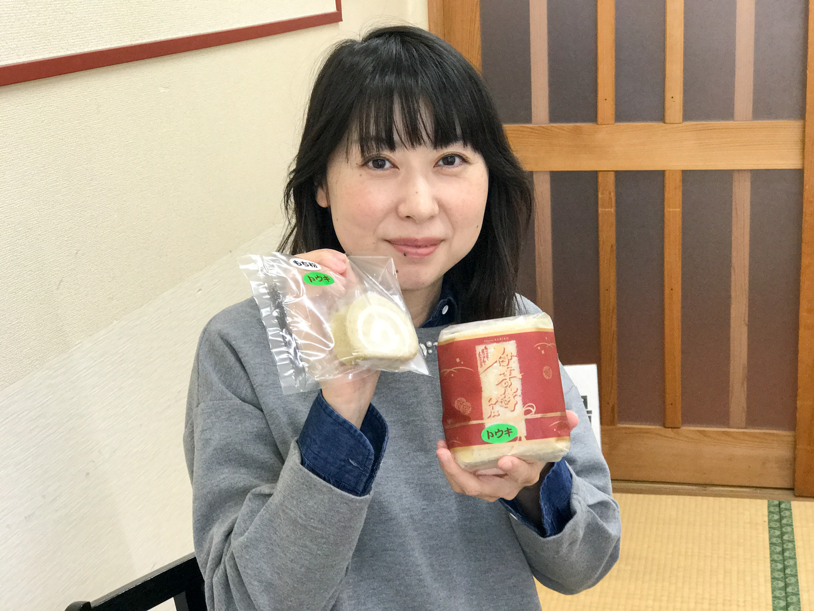 「トウキ」と書かれたシールが貼られたパッケージに入ったロールケーキを両手に持ってカメラに見せている女性の写真