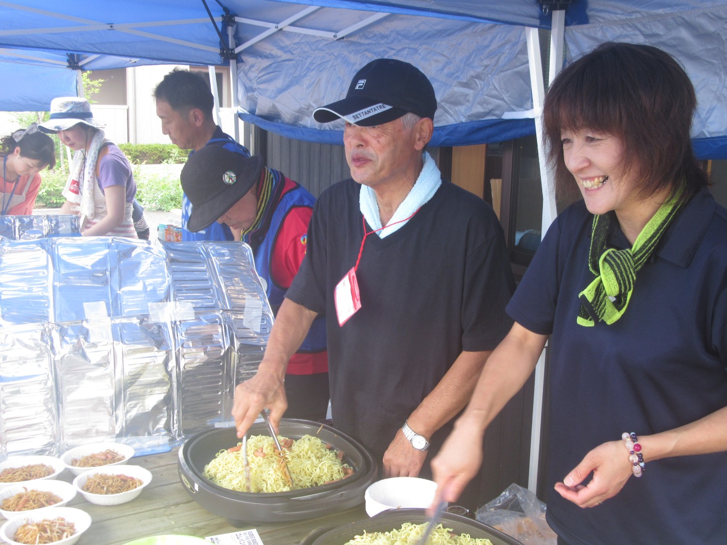女性と男性がホットプレートで汗だくになり焼きそばを作っている様子の写真