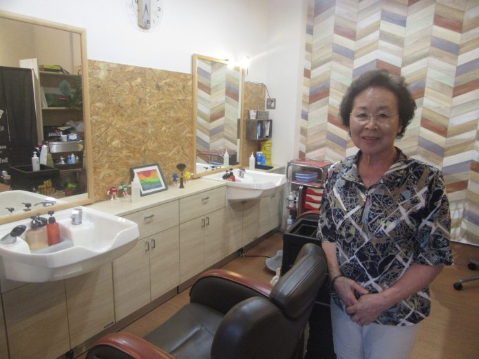 年配の女性が理容室の椅子の横で微笑んで立っている写真