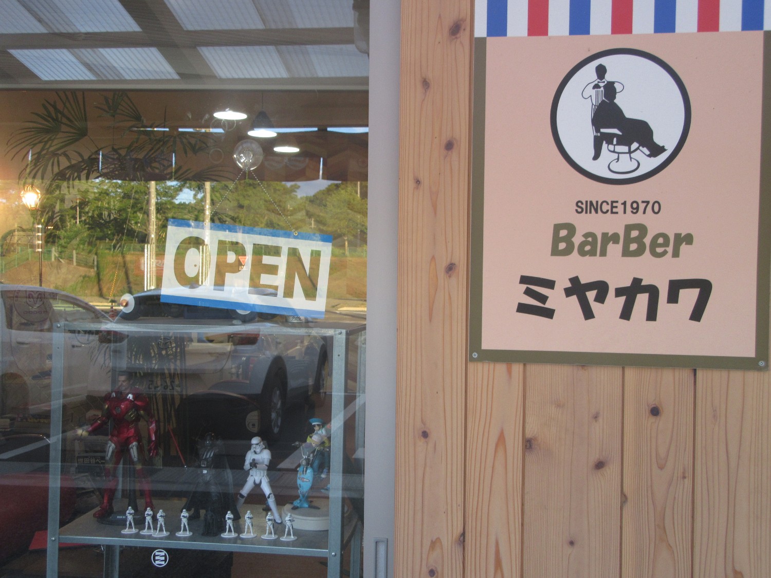 「BarBer ミヤカワ」という看板と、フィギュアが並ぶ理容室のガラス窓に「OPEN」の表示がある写真