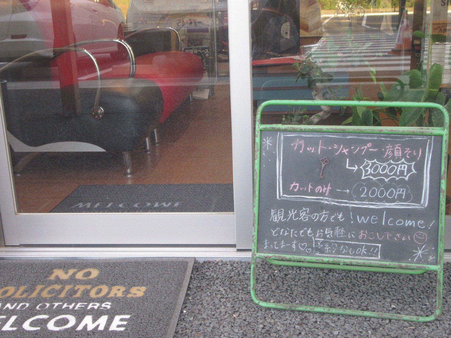 理容室の入口前にカット料金や歓迎メッセージが書かれた黒板が置かれている写真