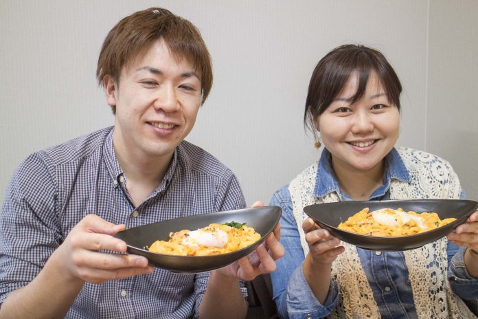 伊藤さんと女性リポーターが並んで麺料理が盛り付けられた黒い器を持って笑顔で写っている写真