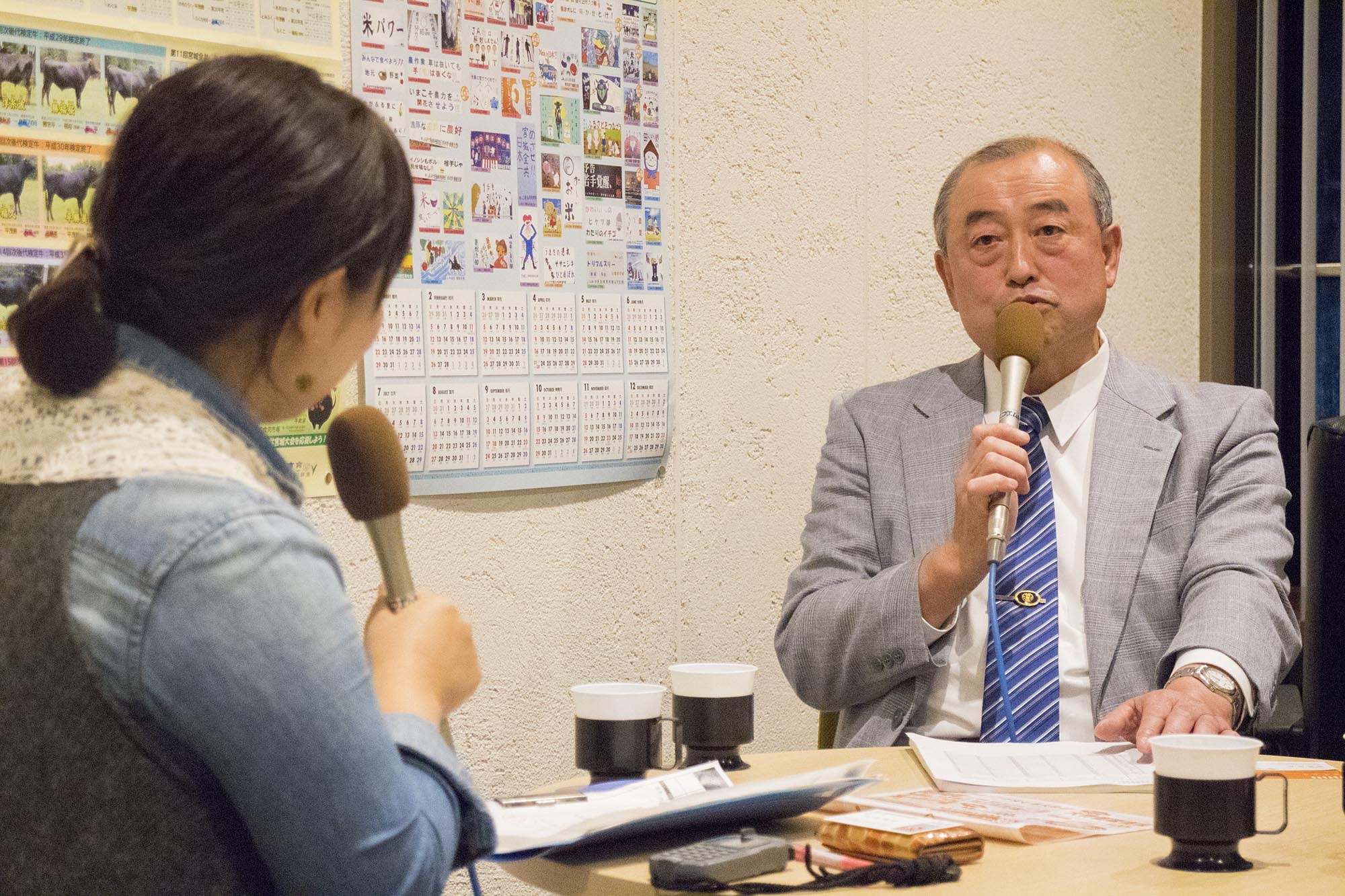 マイクを持った阿部さんと、リポーターの女性が机をはさんで対談している写真