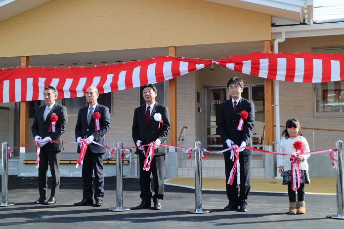 新築された志津川保育所の前で、スーツ姿の関係者4名と白いセーターを着た女の子が並び、赤白のテープをハサミで切って開所を祝うテープカットの様子を写した写真