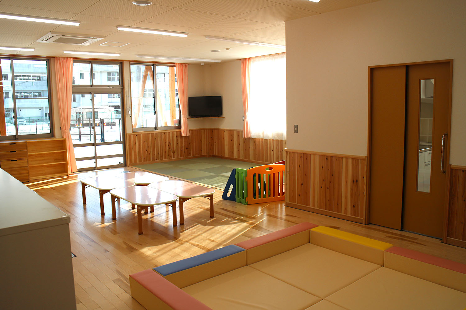 日の光が差し込む大きな窓や畳スペース、低いテーブルやクッションマットがあり、木の温もりが感じられる志津川保育所の保育室の写真