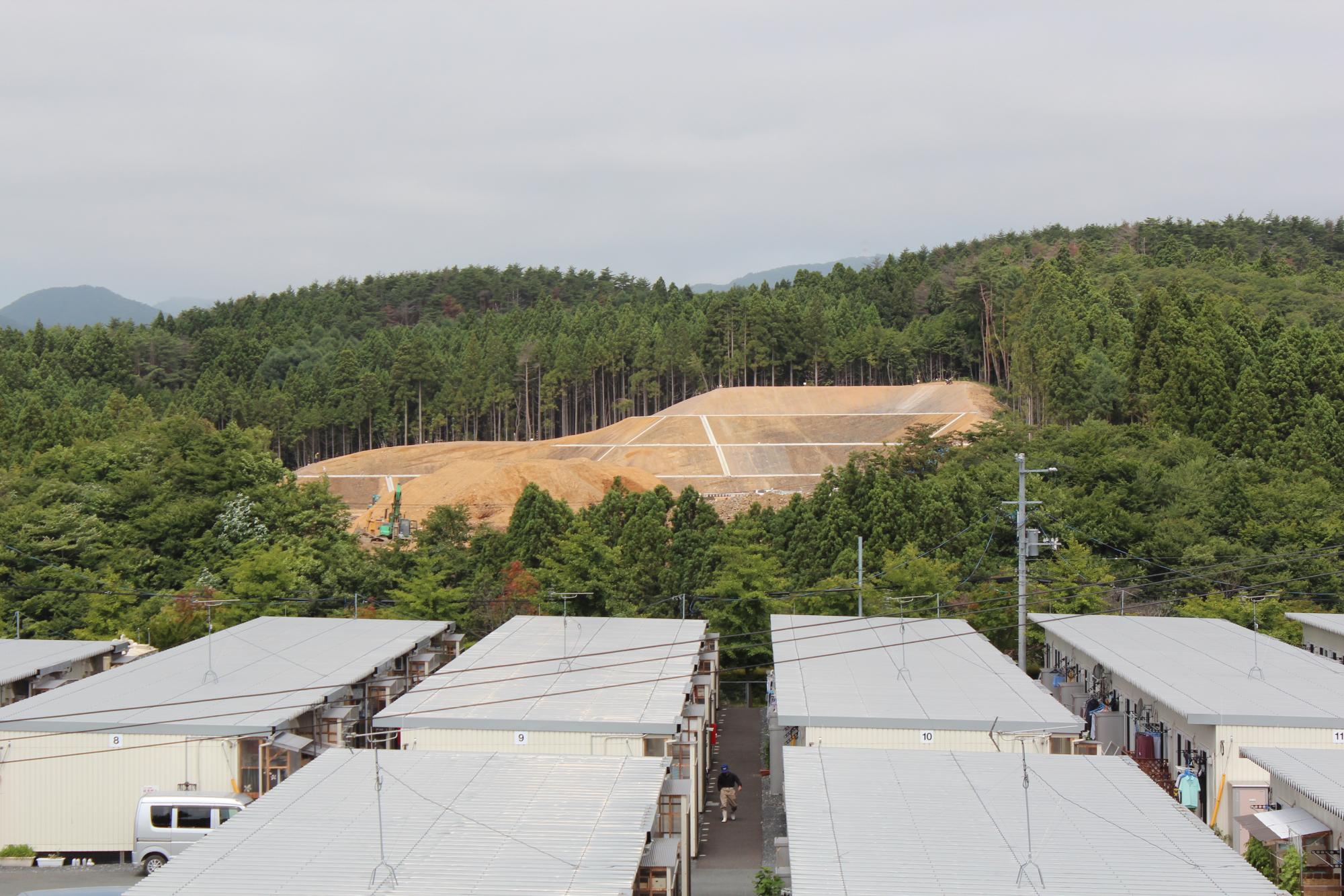 仮設住宅群の背後で重機を使った高台造成が進む様子を示す写真