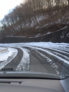 道の両脇にガードレールと雪をかぶった斜面が見え雪が部分的に残る山道の急カーブを車の中から撮影された写真