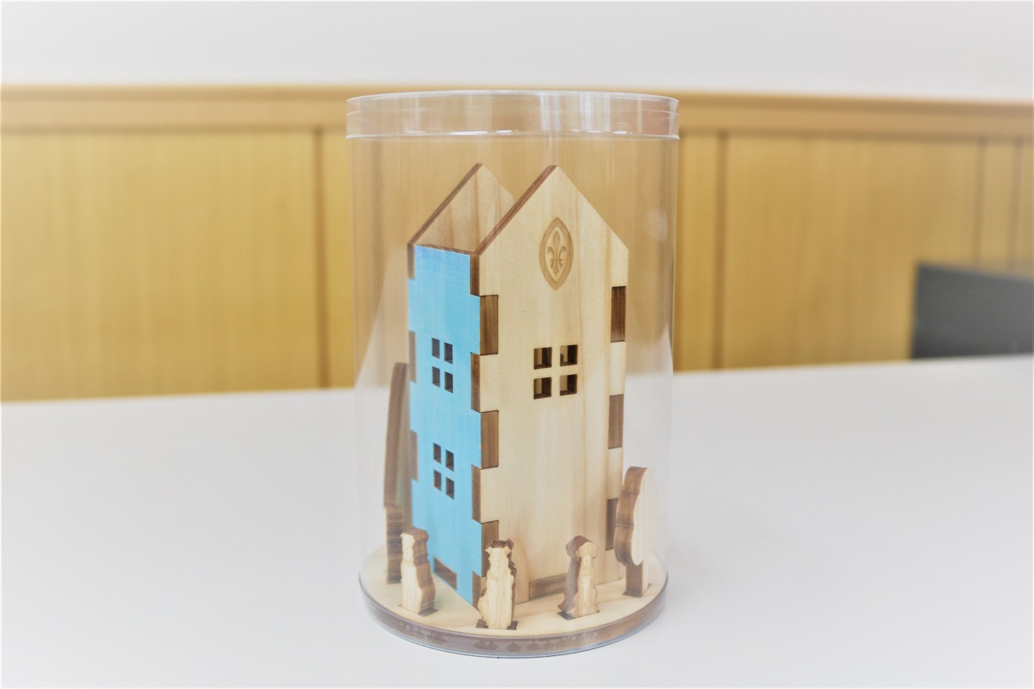 水色の壁と動物や木のミニチュアが飾られた木製の家型ペンスタンドが透明な筒に入っている写真