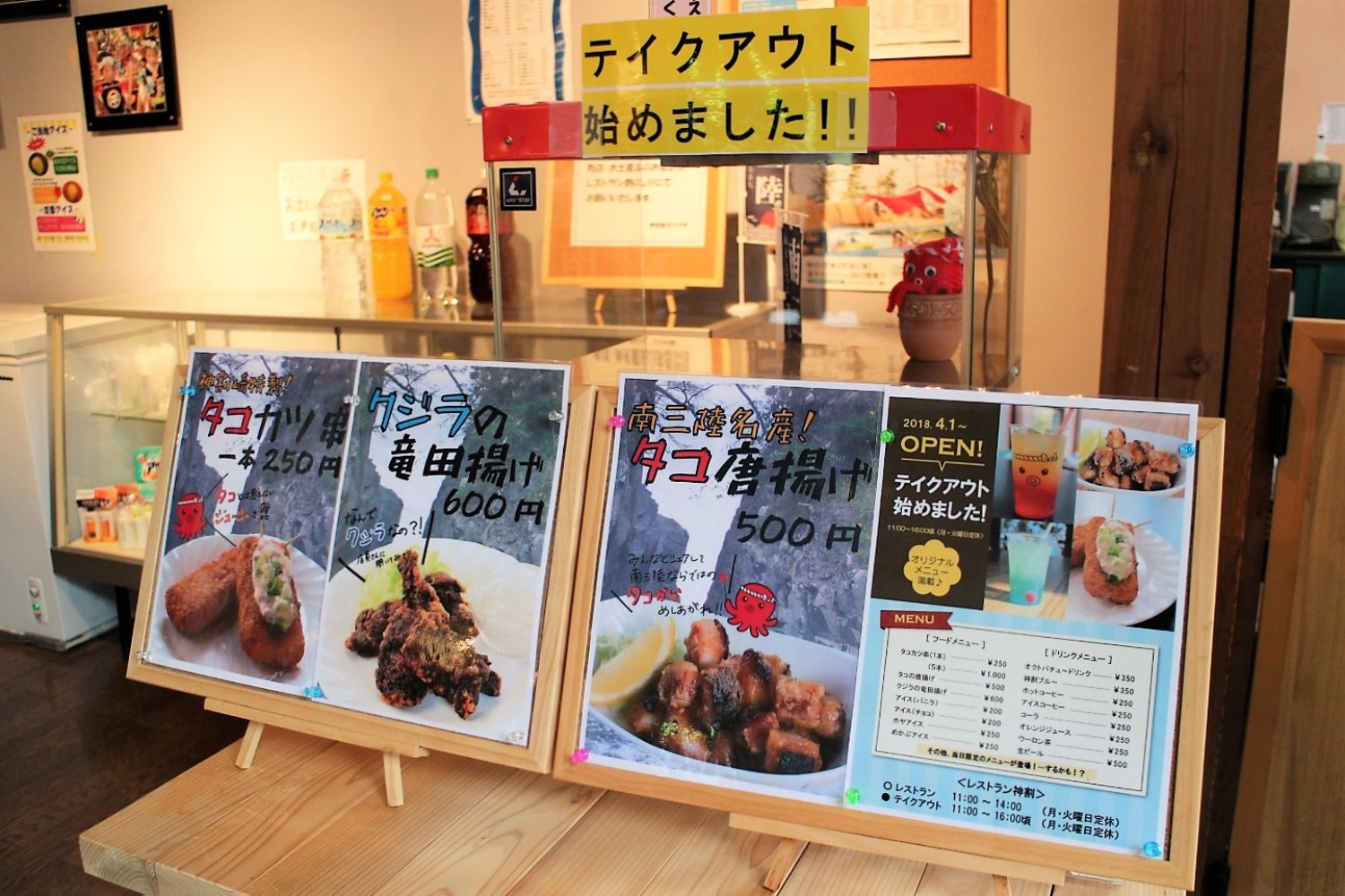 店舗カウンターに並んだ、タコカツやクジラの竜田揚げなどの写真付きメニューが並ぶテイクアウトコーナーの写真