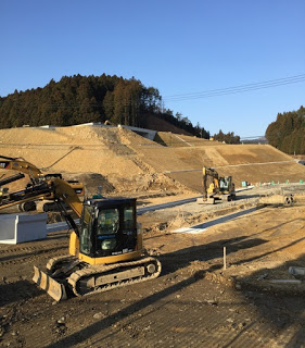 山のように積まれた土の斜面の下で複数の重機が工事作業を行っている様子の写真