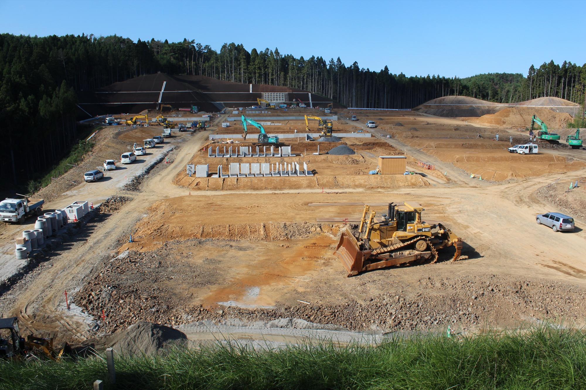 整地が進み、複数の重機と車両が資材を搬入している造成現場の写真