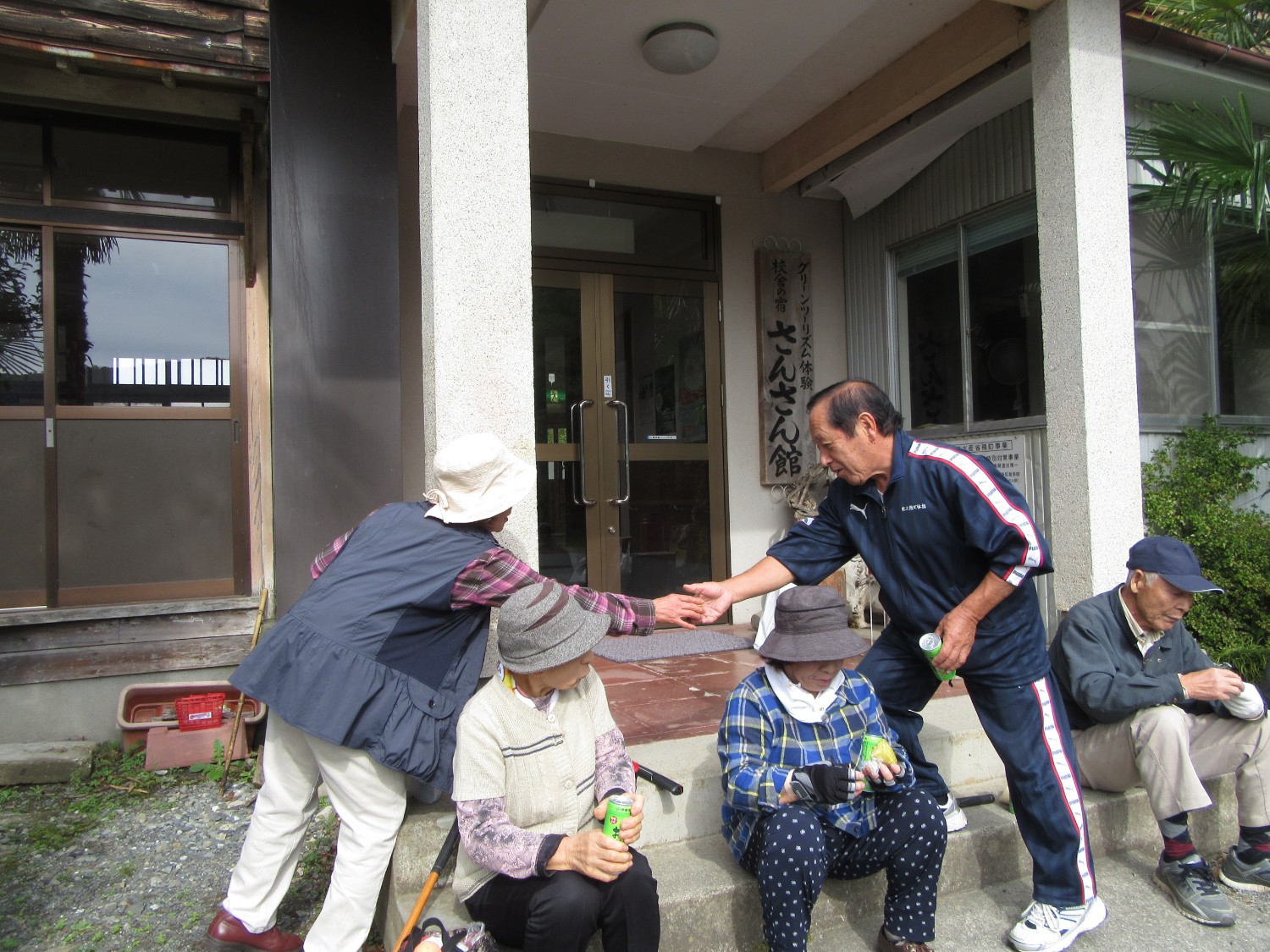 さんさん館の建物入り口前に腰掛けお茶を飲んでいる高齢者たちの写真