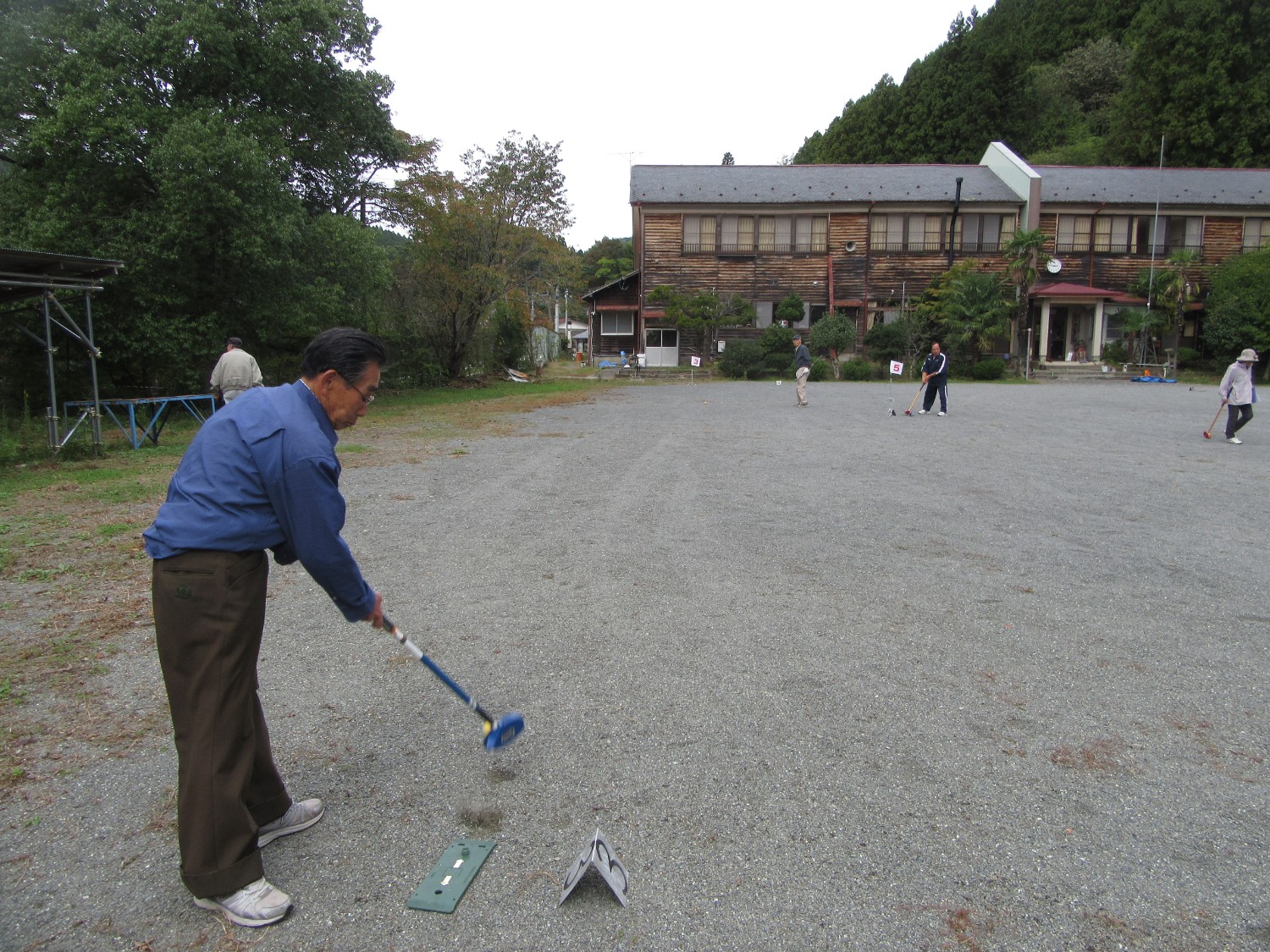 屋外の広いグラウンドで、複数の高齢者がゲートボールを楽しんでいる写真