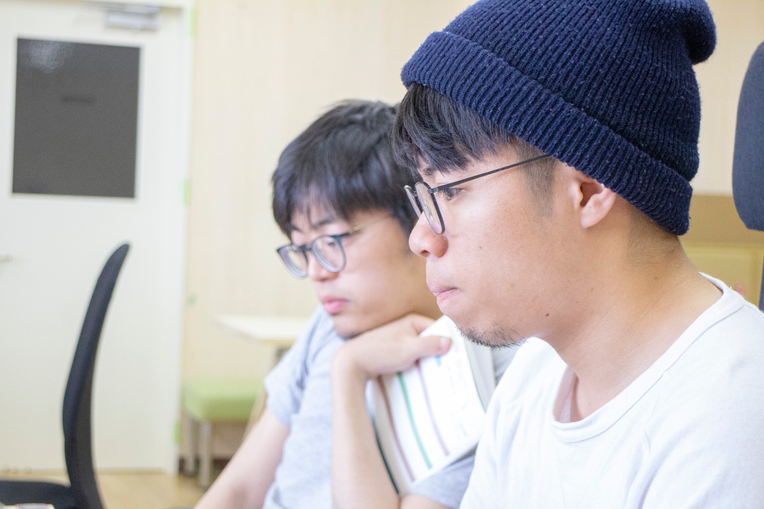 平山さんが真剣な表情で画面を見つめ、隣の男性と共に集中して作業している写真