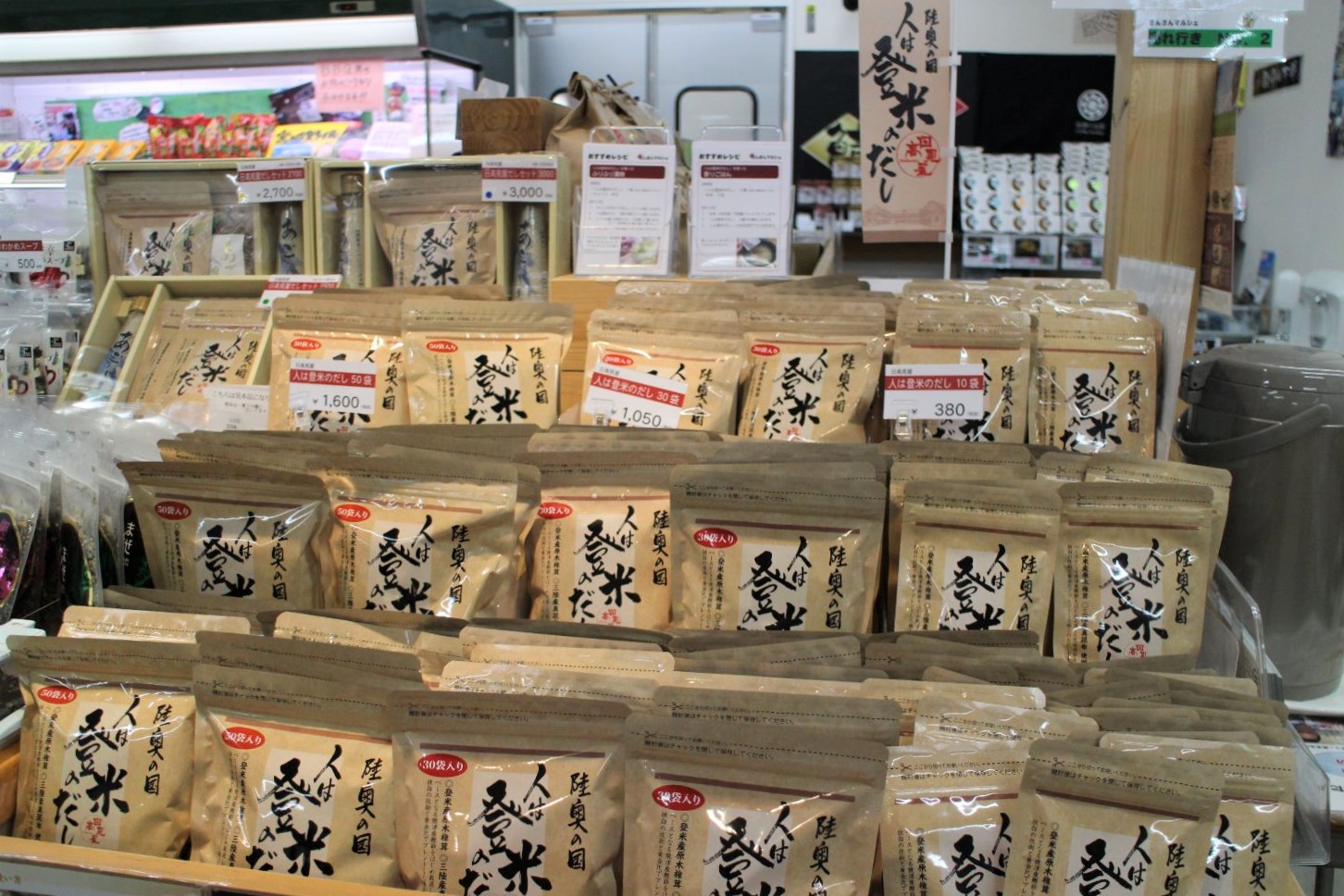 ベージュ色のパッケージに「人は登米のだし」と書かれた商品が3段の陳列棚に並んでいる写真