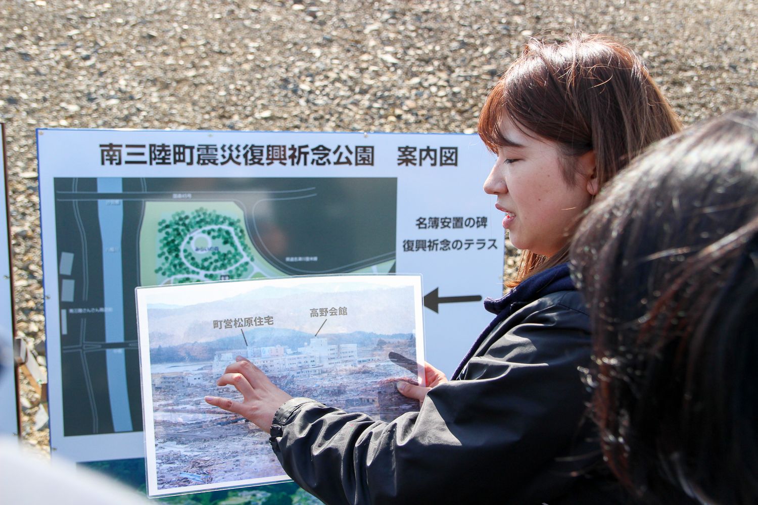 若い女性が震災直後の被害を写した写真を指さしながら、後ろの地図とともに説明している写真