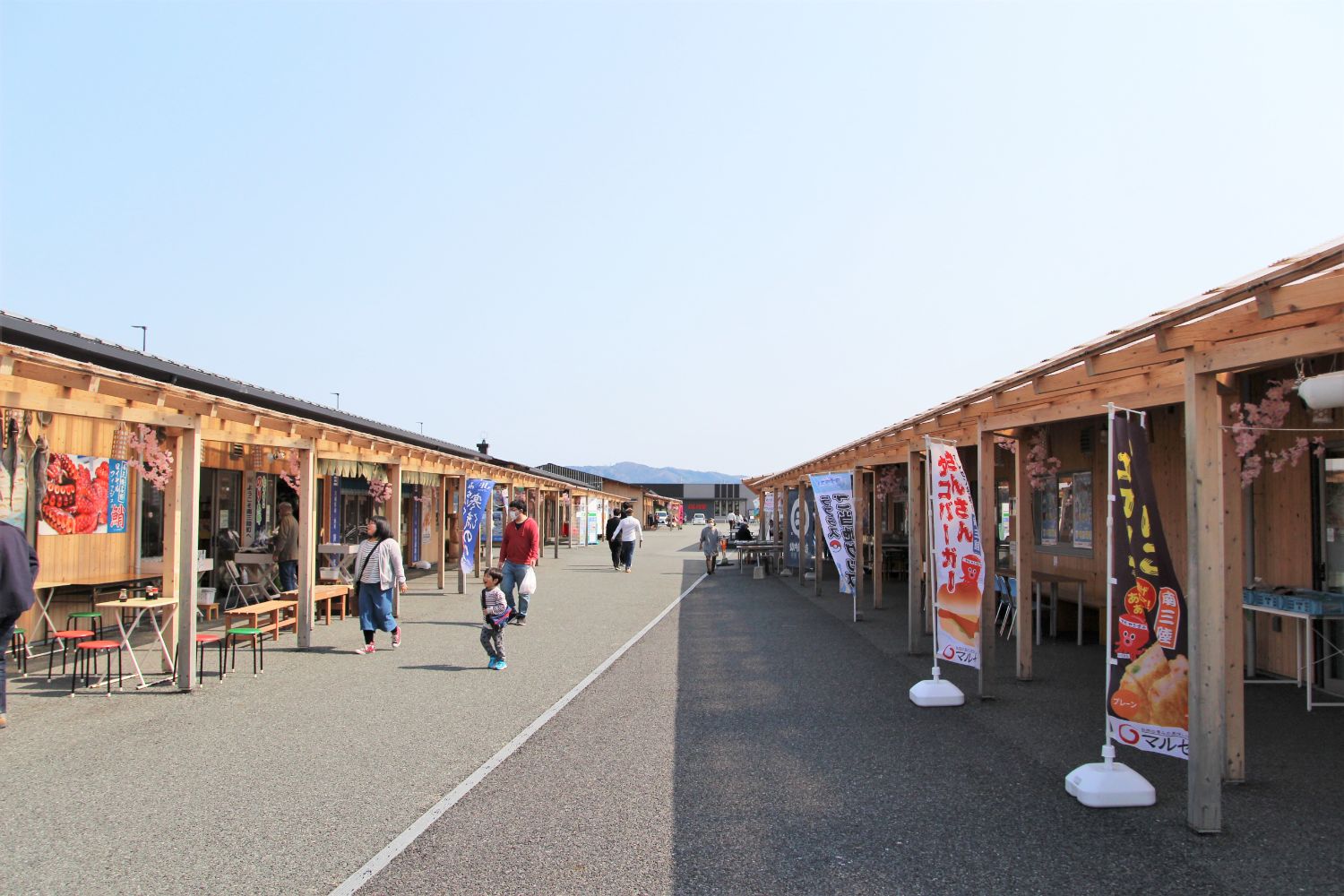 木造の屋台風の店舗が両側に並び、親子連れや買い物客が行き交う穏やかな雰囲気のさんさん商店街の写真