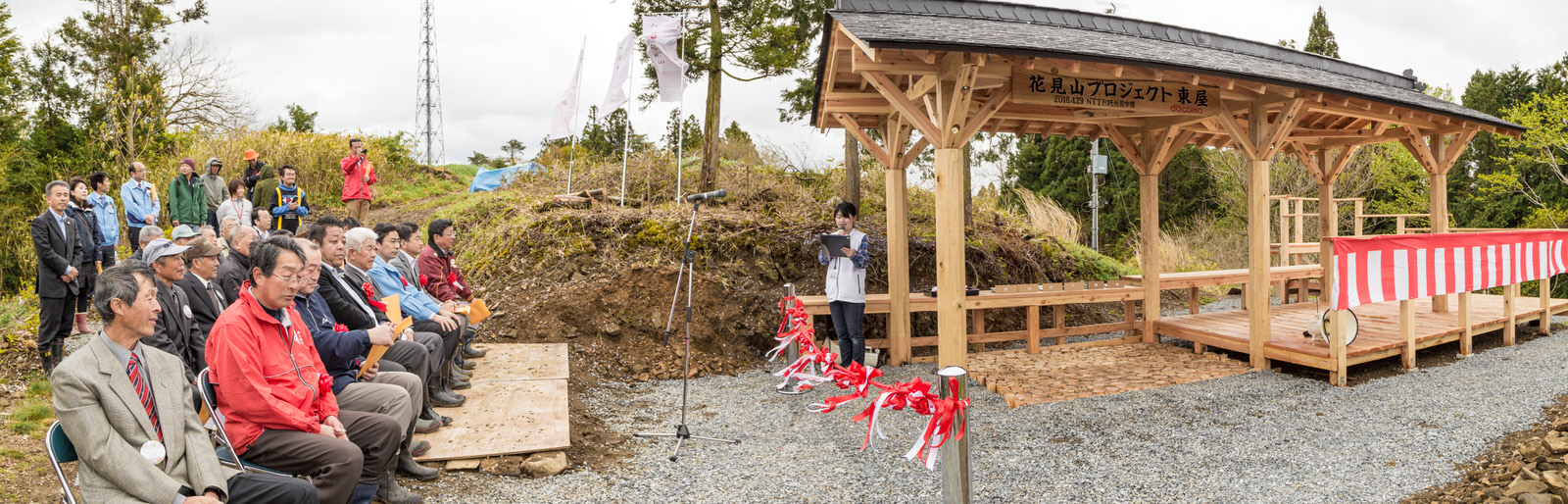 完成した東屋の横に紅白幕、手前に紅白のテープが設置され、並んだ椅子に大勢の関係者が座り、その後ろにも関係者の方々が立っているセレモニー時の写真