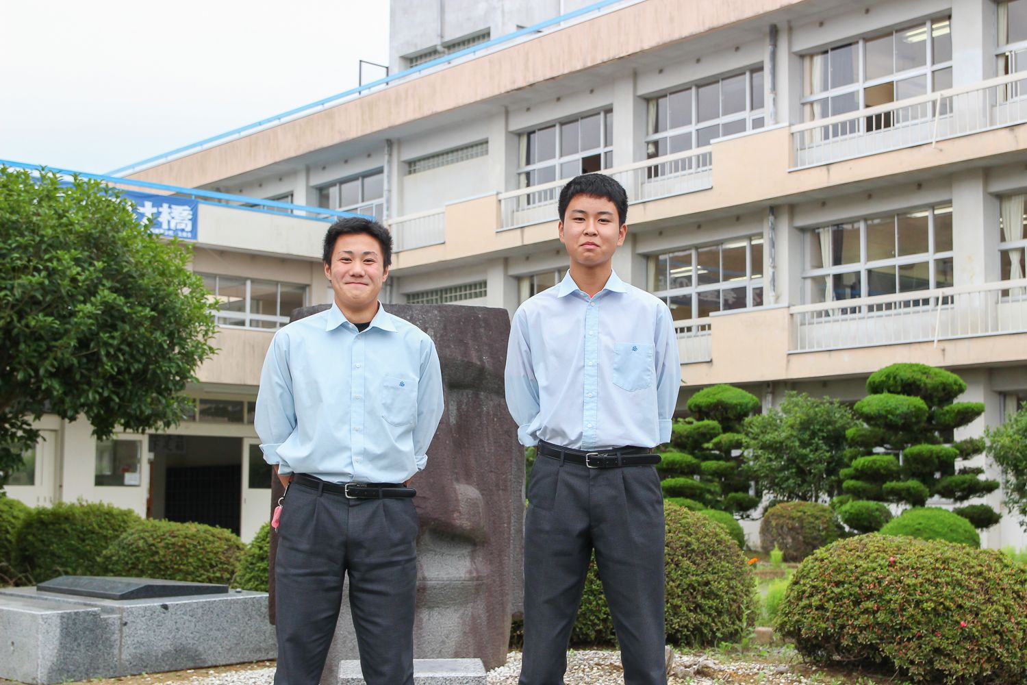 校舎の前に制服姿の及川拓海さんと木下巧大さんが立っている写真
