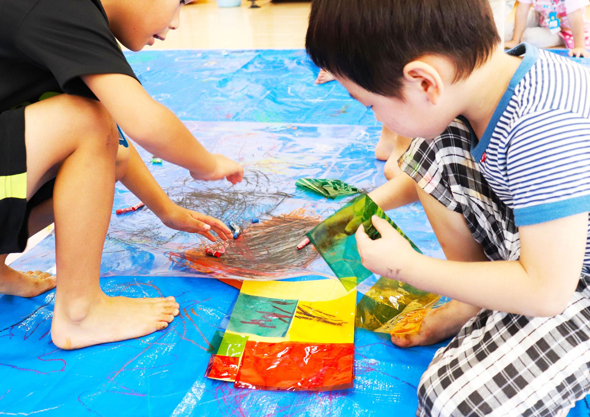 透明シートにクレヨンで絵を描き、シートの下に色画用紙を入れて変化に興味を持つ子供達の写真