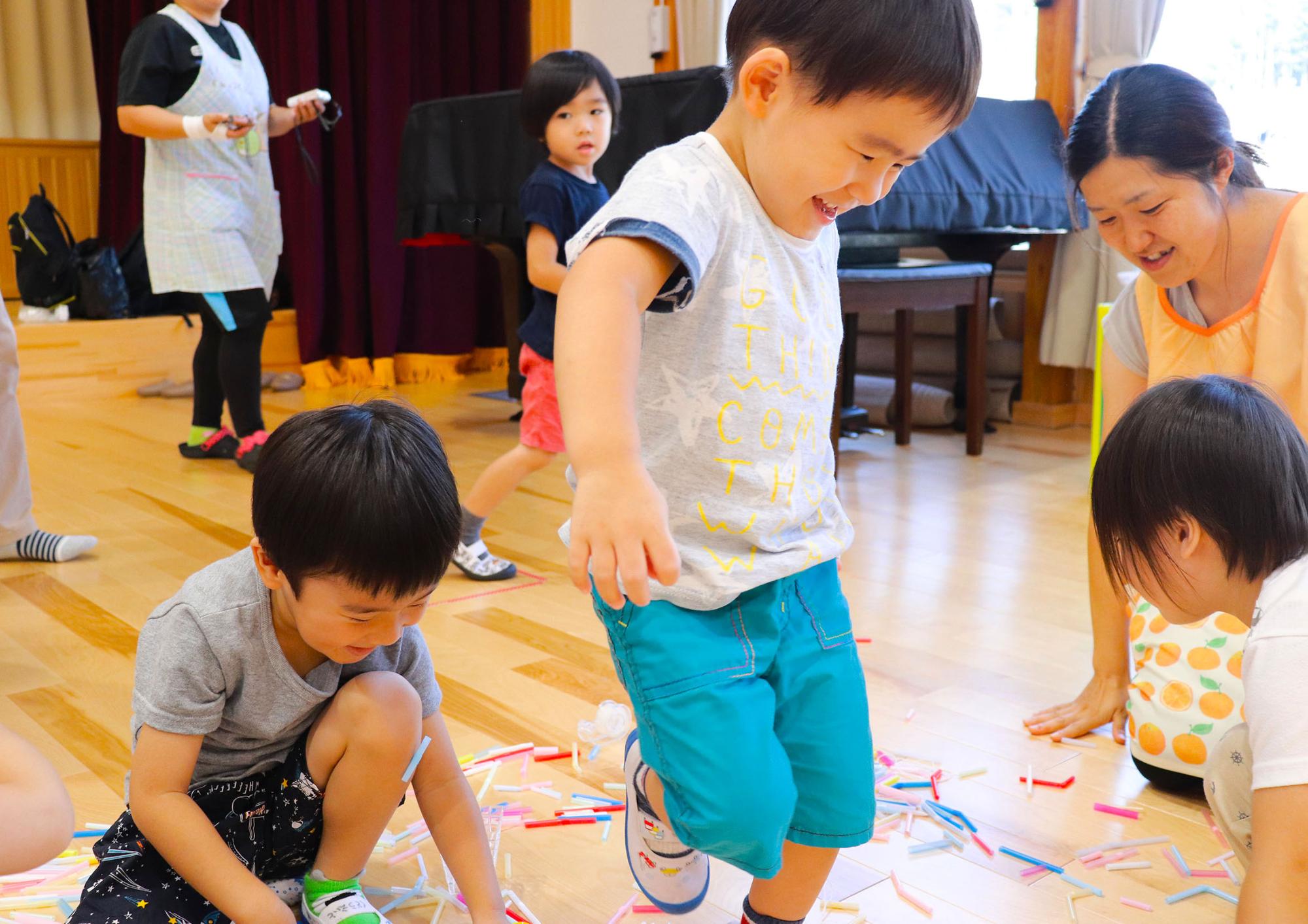 床の上でカラフルなストローを繋げて作った作品ではしゃいでいる子供達の写真