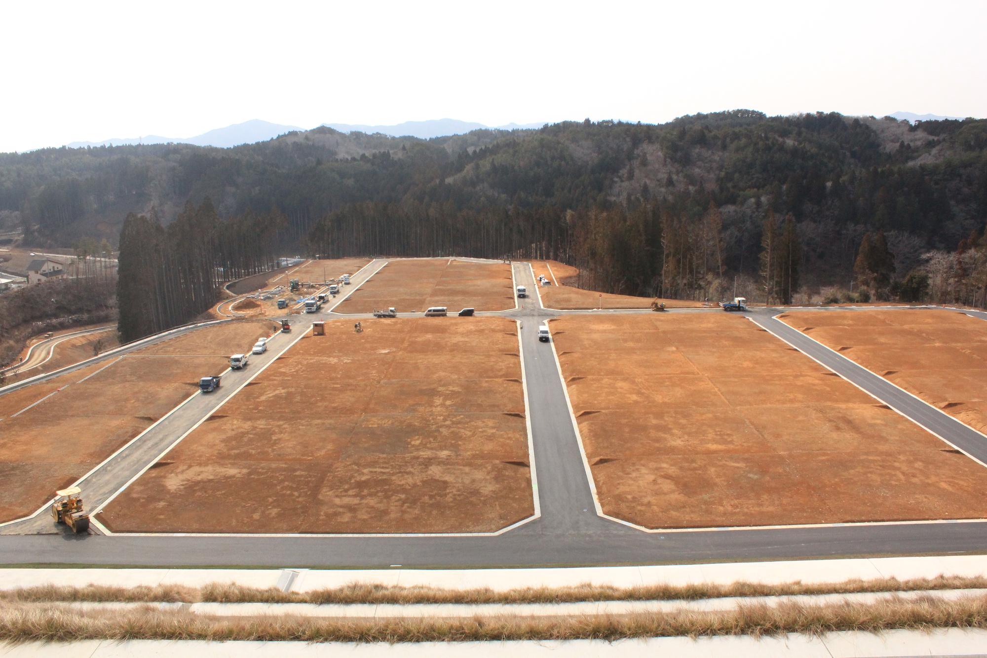山を切り開いて整地された広大な宅地予定地が整然と区画されて並び、周囲には沢山の工事車両が道路を均した作業が進められた完成間近の造成地の写真
