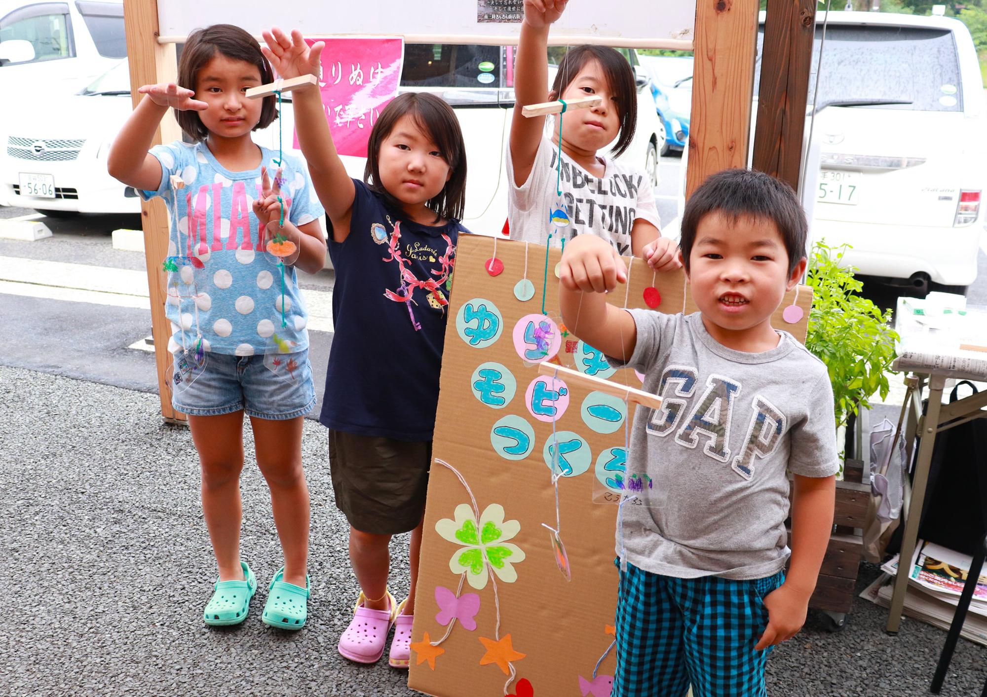 4人の子どもたちが、自分で作ったカラフルなモビールを手に持ってポーズをとっている写真