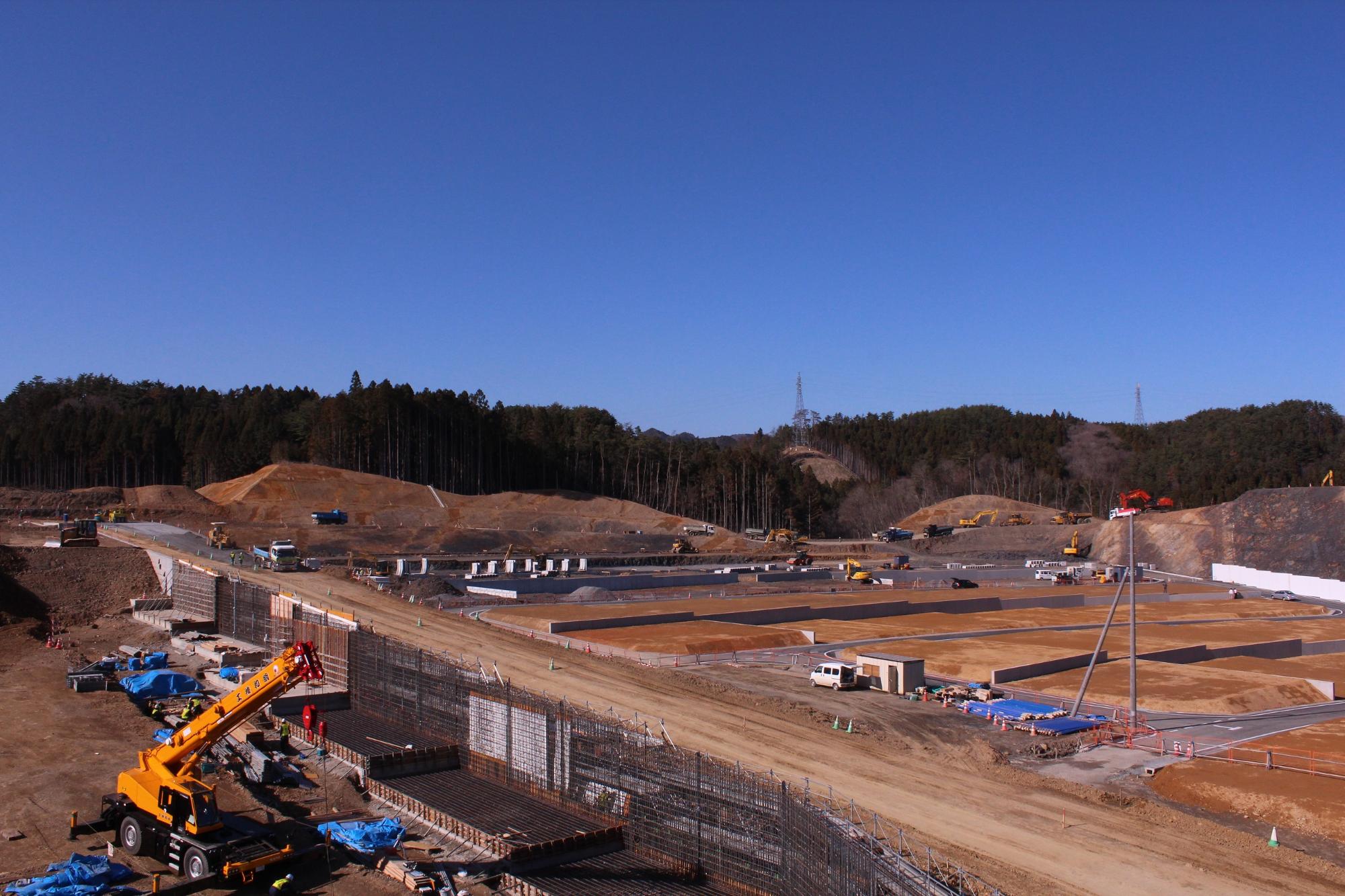 青いシートで覆われた資材置き場があり、スロープや区画道路の骨組みが完成しつつあり、宅地の枠組みが明瞭になってきている写真