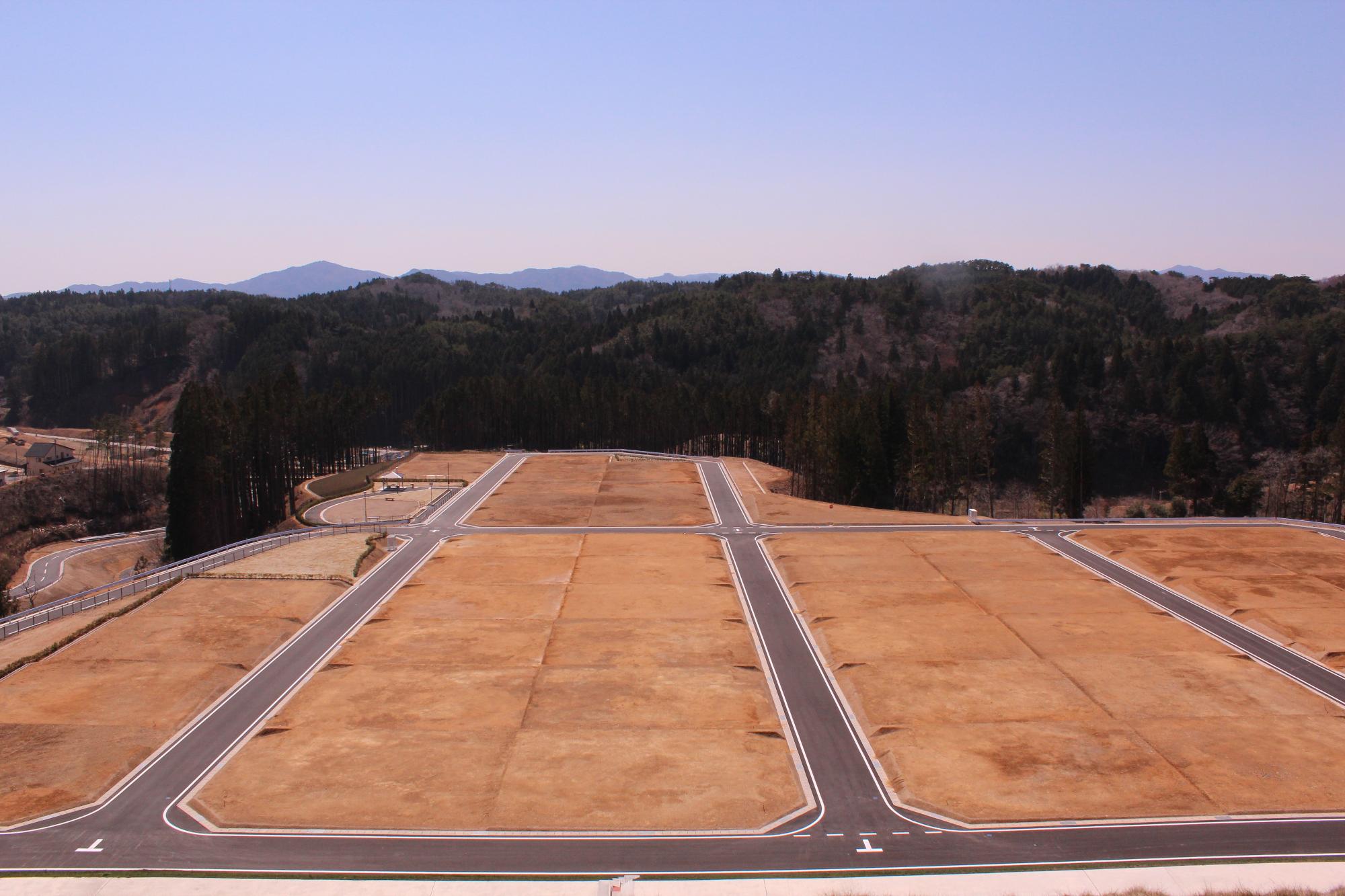 山を切り開いて整地された広大な宅地予定地が整然と区画されて並び、背景には山々が広がっている完成した宅地造成地の写真