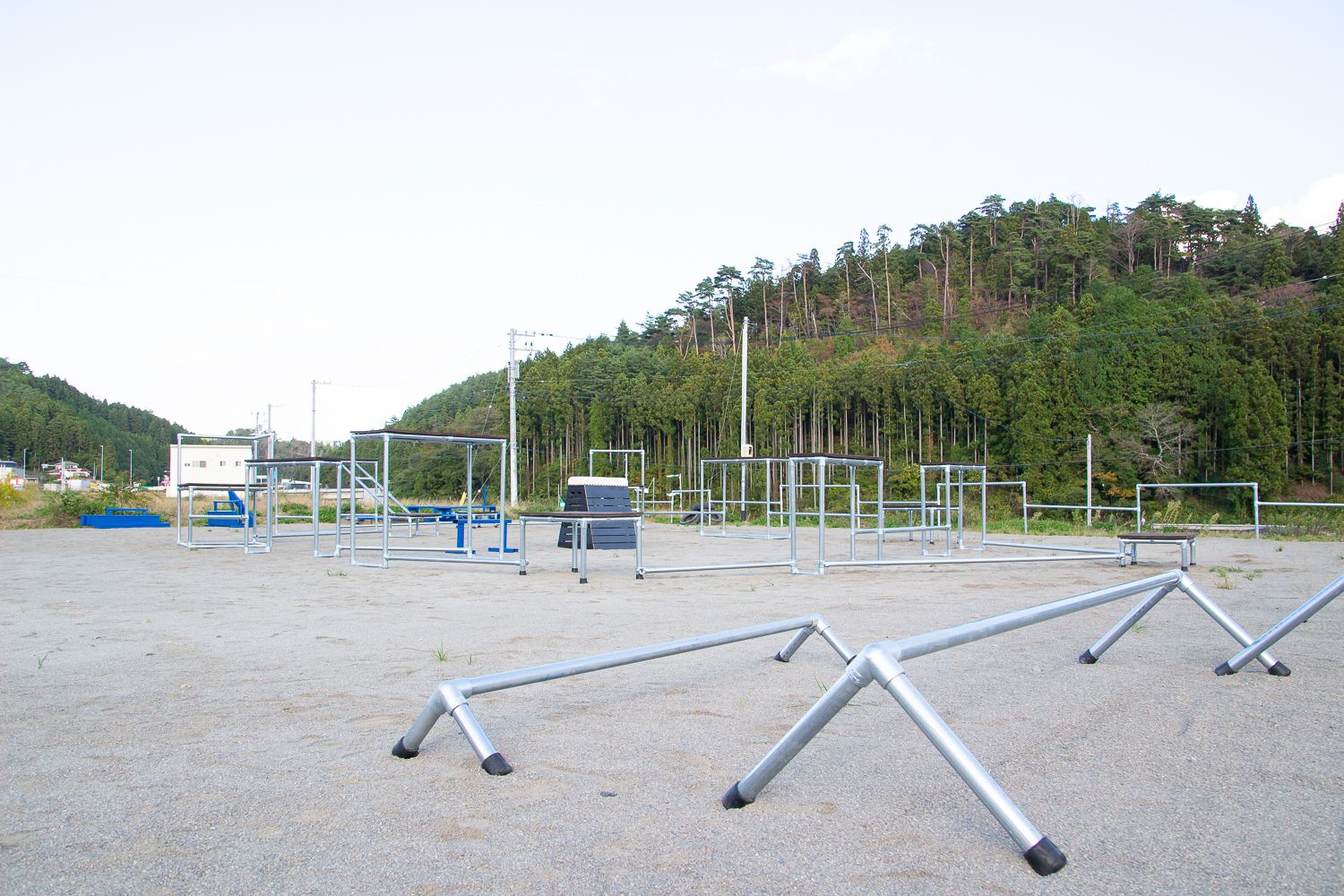 広い砂地の地面に、鉄パイプで組まれた形は四角形や三角形のフレームで高さは地面すれすれの低いものから、大人の背丈よりも高さのあるパルクールの写真