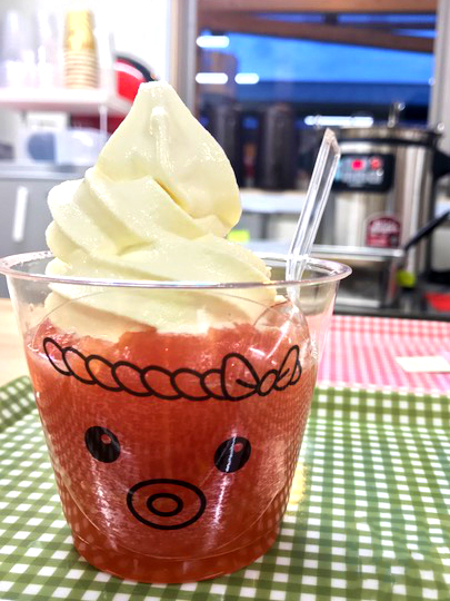 ねじり鉢巻きを巻いたタコの顔が描かれた透明のカップに入った赤いトマトのコンポートにソフトクリームが乗り、スプーンが添えられたタコソフトクリームの写真