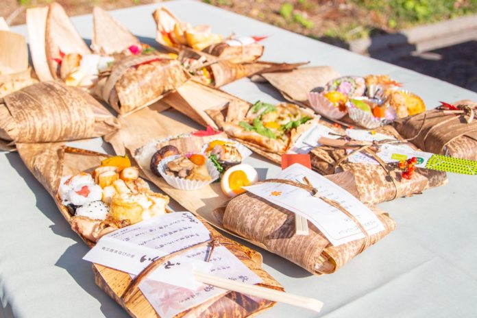 竹の皮で包まれた色とりどりの中身の違う手作り8種類の弁当が広げられ2列に並べられている写真