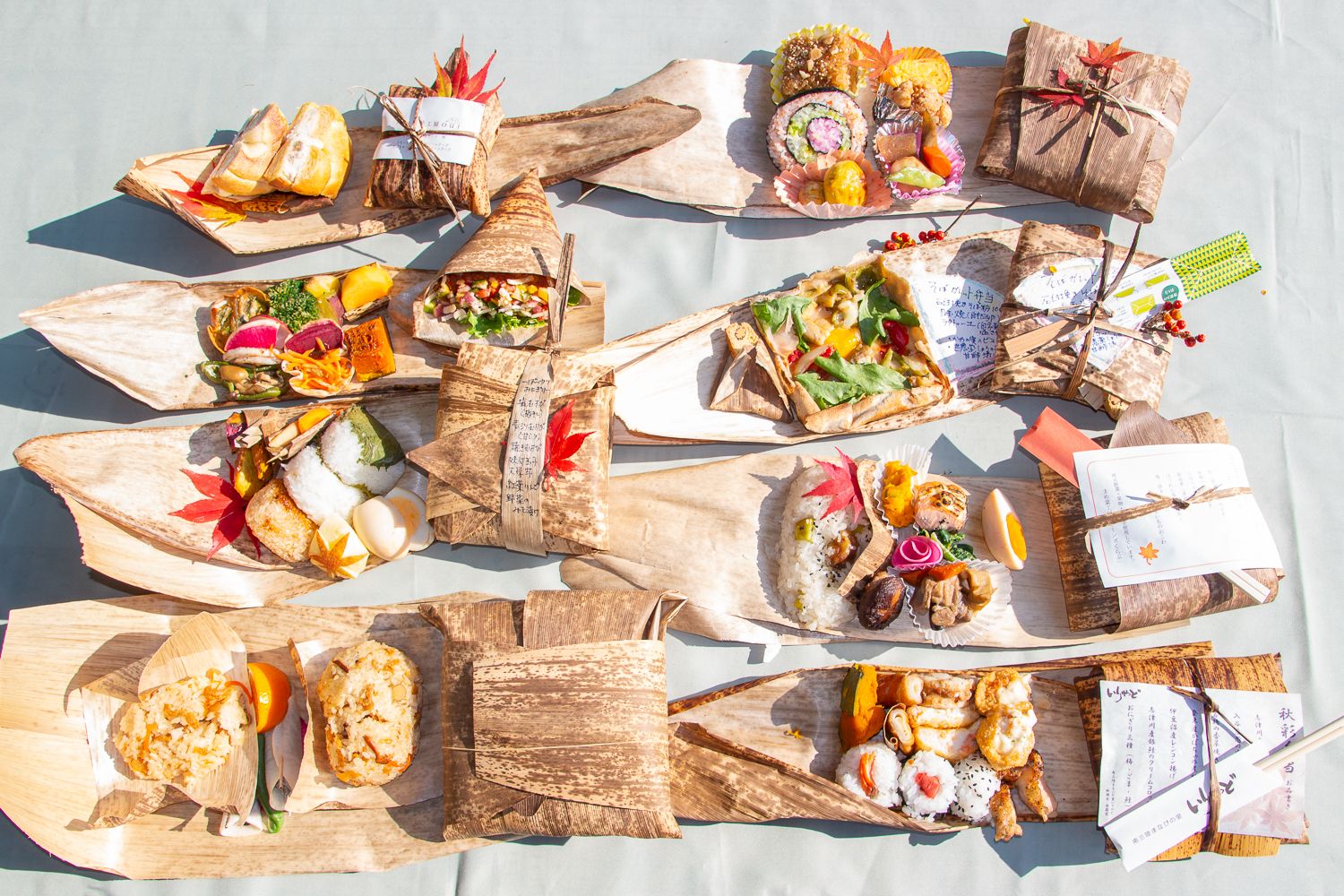 竹の皮の上に彩り豊かな美味しそうなお弁当が丁寧に盛られ中身を見せ2列並んでいる写真