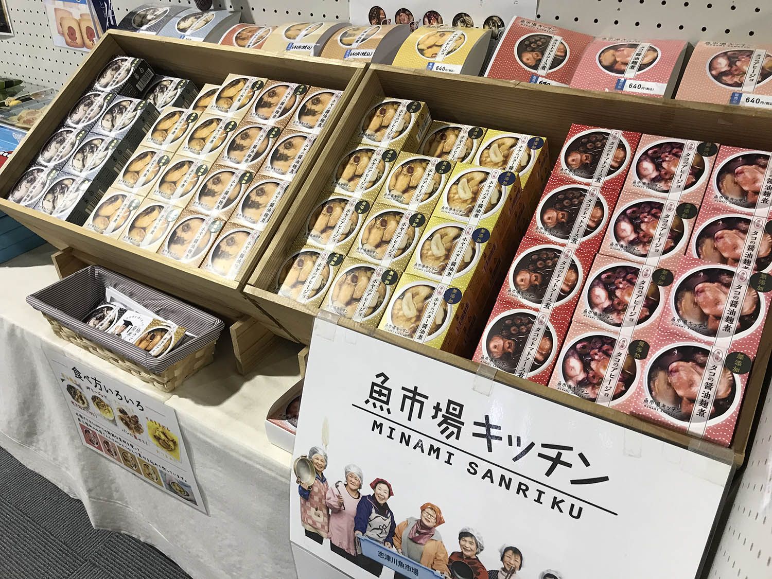 「魚市場キッチン MINAMI SANRIKU」と書かれたポップが貼られたテーブルの上に、色とりどりの魚介類の缶詰商品が展示され並んでいる写真
