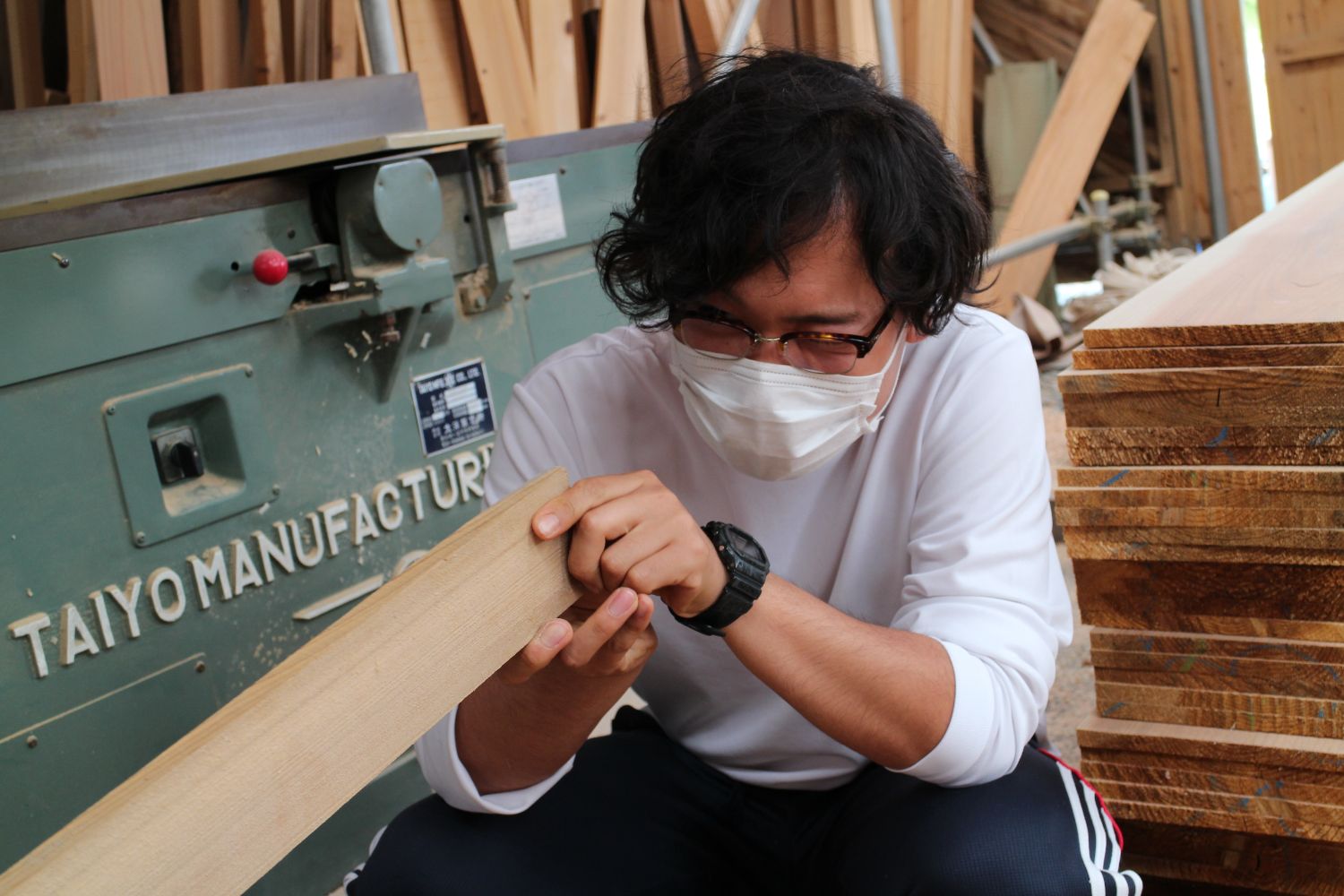 白い服を着た熊谷さんがマスクをして木材を手に取り、目を凝らして表面を丁寧に確認している写真