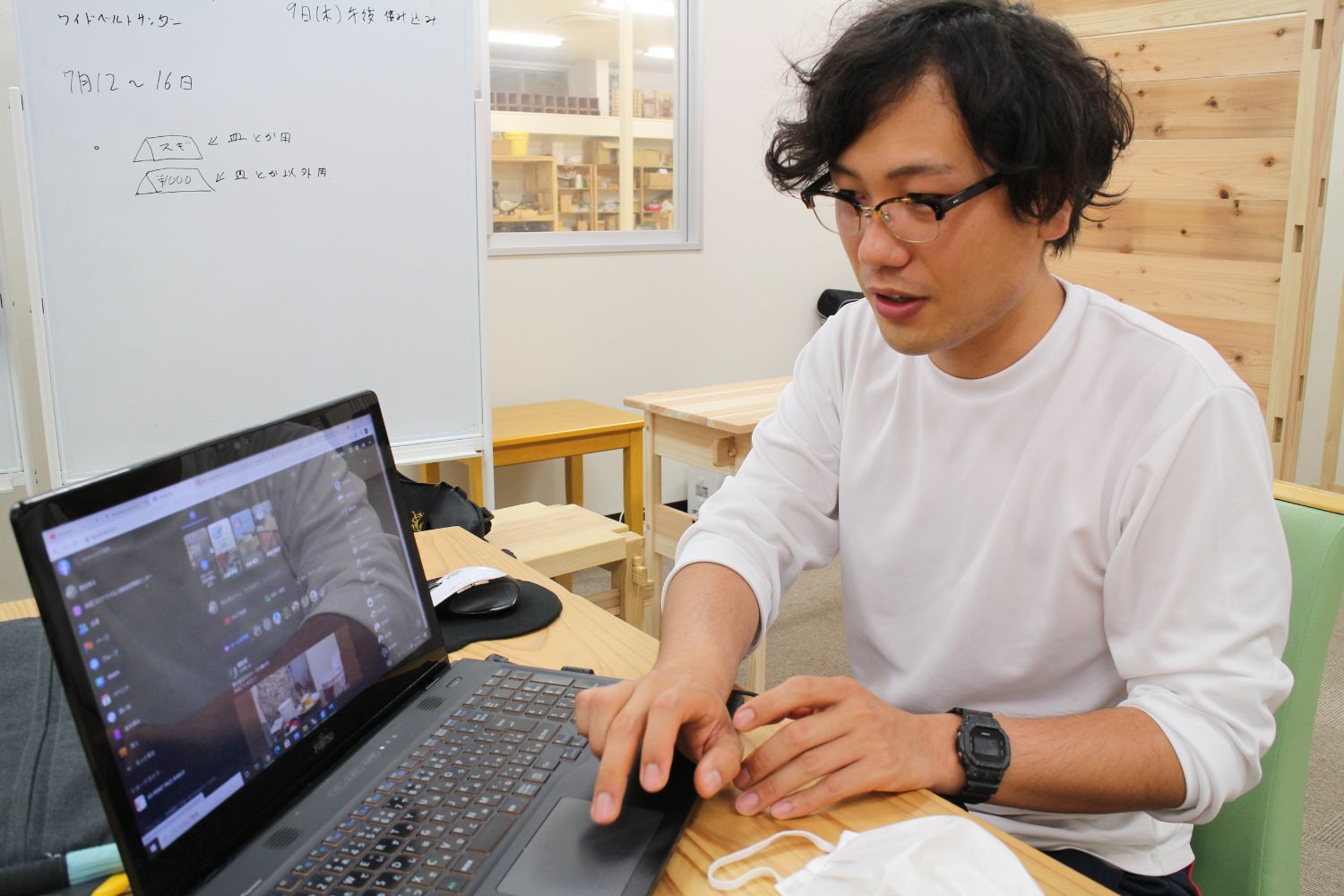 白い服を着た熊谷さんが作業場でパソコンの画面をカメラに見せパソコンの操作している写真