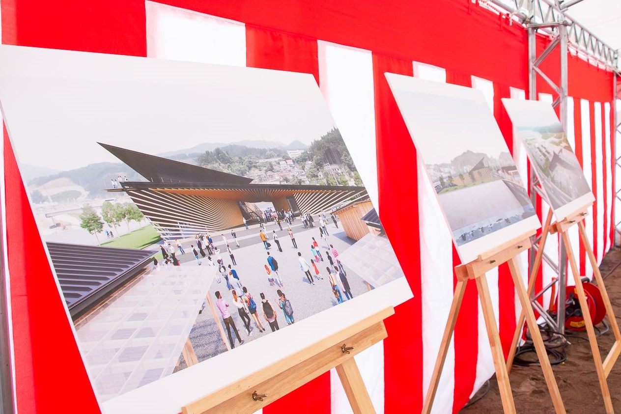 紅白幕が貼られた安全祈願祭会場で、それぞれが人々が行き交う近代的な建物の異なる視点からの三枚の大きな道の駅の完成予想図が木製のイーゼルに立てかけられ展示されている写真