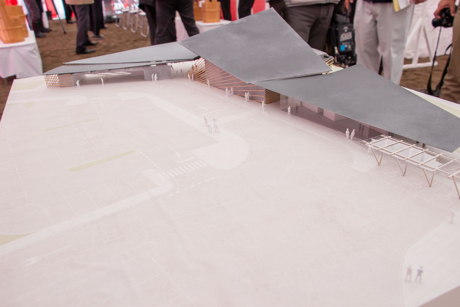 安全祈願祭の場に設置されたテーブルの上に、周囲に広い空間や通路、小さな人形が配置され、大きく角ばった2重の屋根を持つ道の駅の建築模型の写真