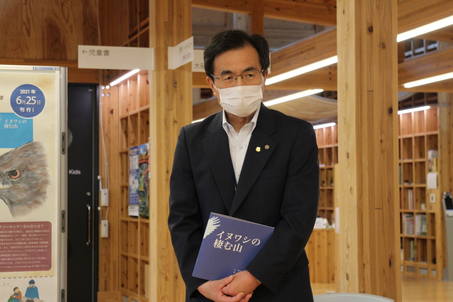 南三陸町生涯学習センターでスーツを着た齋藤明さんが絵本『イヌワシの棲む山』を手に持っている写真