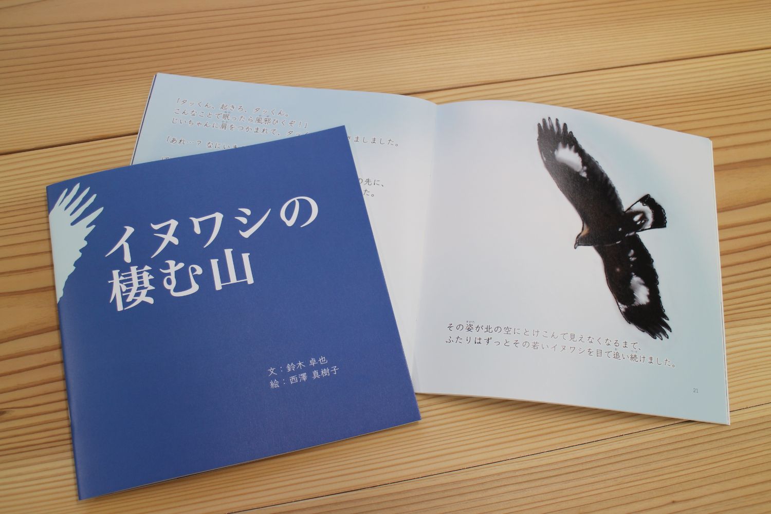 木の机の上に、絵本『イヌワシの棲む山』が開かれた状態で置かれており、表紙とともに、中面には大空を羽ばたくイヌワシの写真と優しい語り口の文章が印刷された絵本を写した写真
