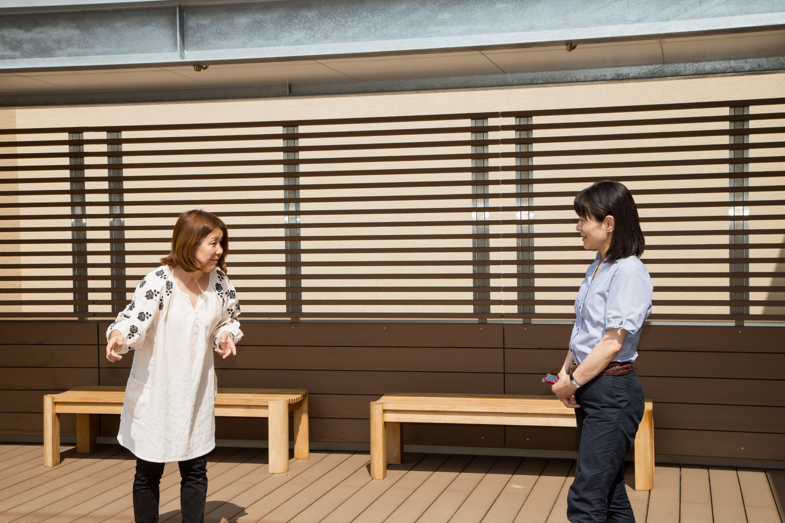 ベンチが2つ並べられ、目隠しフェンスがついたウッドデッキで佐々木千夏先生と筆者の女性が話をしている写真