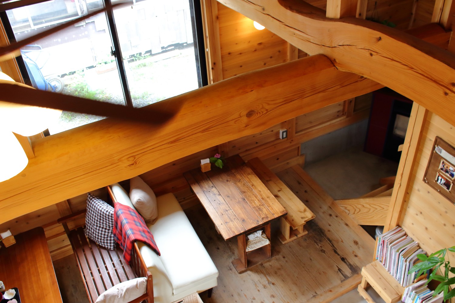 木製のテーブルと椅子が配置され、クッションやブランケットが置かれている木の柱と梁がむき出しになった温かみのある店内の写真