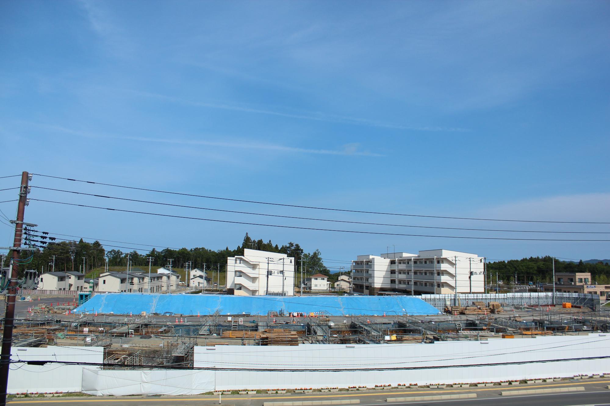 多数の鉄骨や建設資材が整然と並べられ、青いシートが斜面にかけられた建設中の平成28年6月7日現在の写真