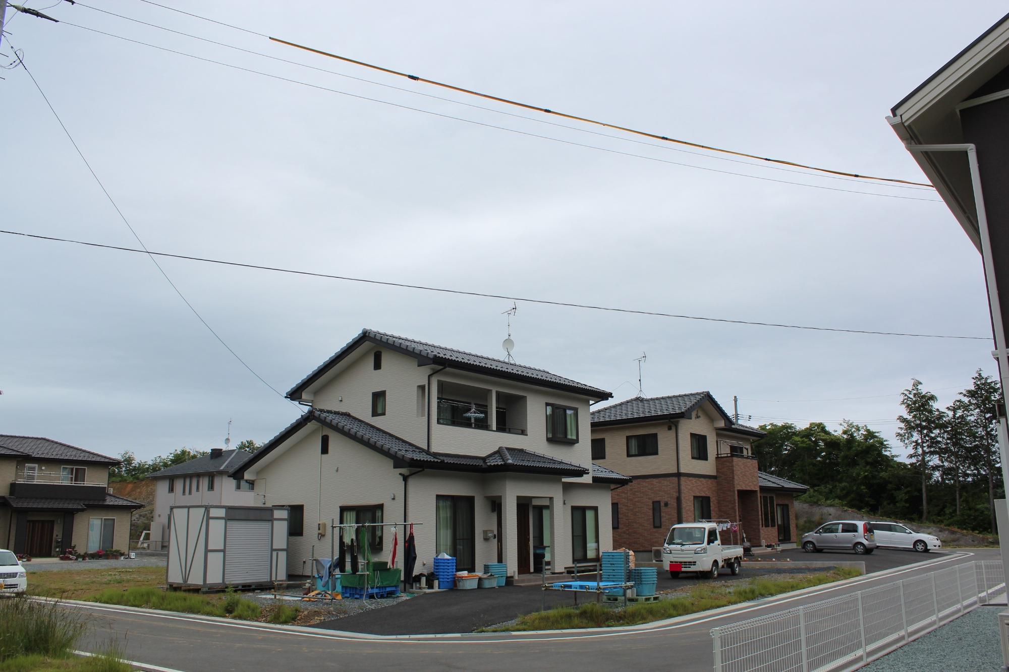 新しく造成された住宅地に、白やレンガ調の二階建て住宅が整然と建ち並び、敷地内では洗濯物が干され軽トラックが停まっている写真