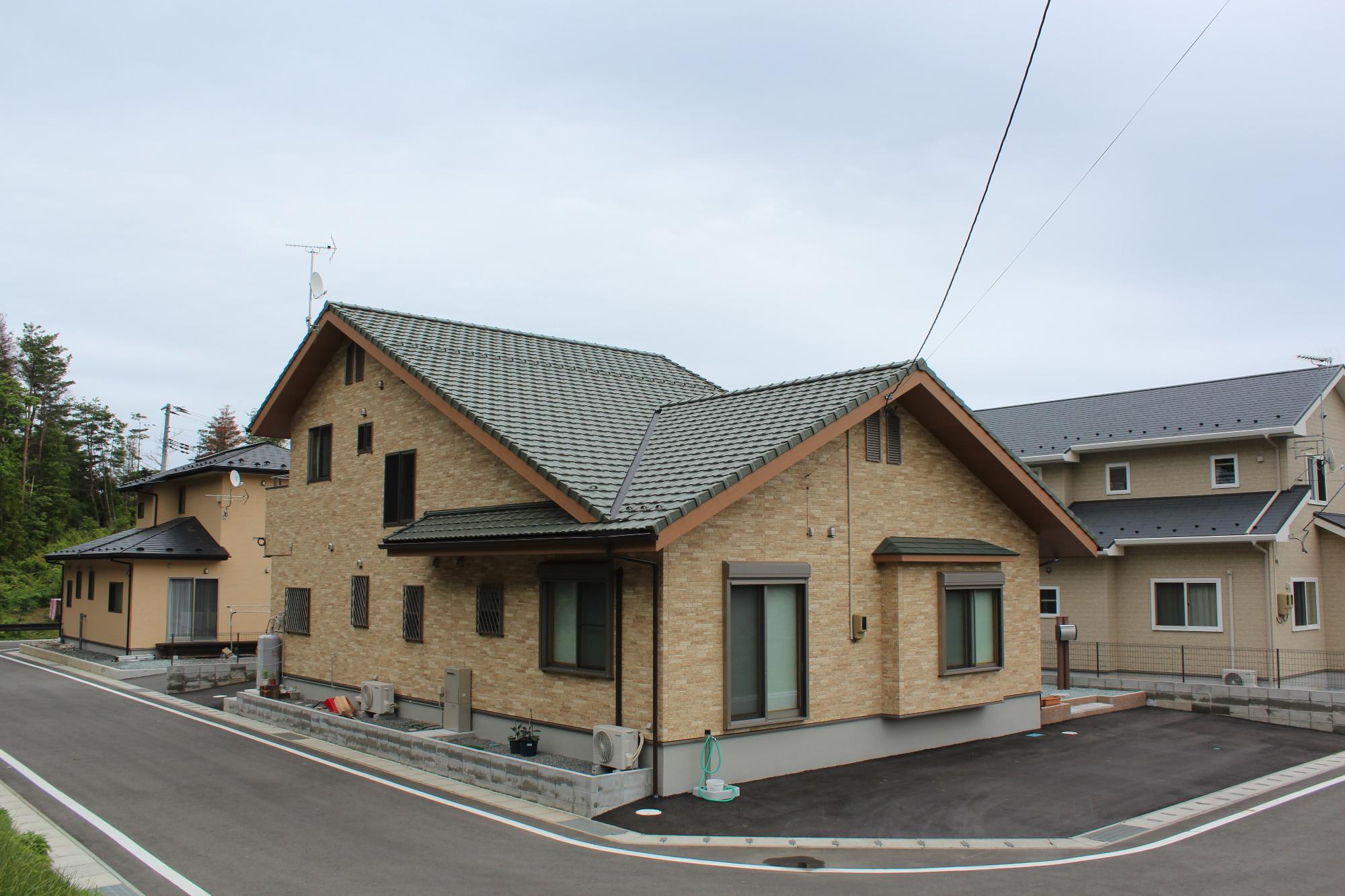 落ち着いた色合いのタイル張りの平屋建て住宅が角地に建ち、周囲には舗装された道路と整備された駐車スペースがある、住宅街の一角の写真