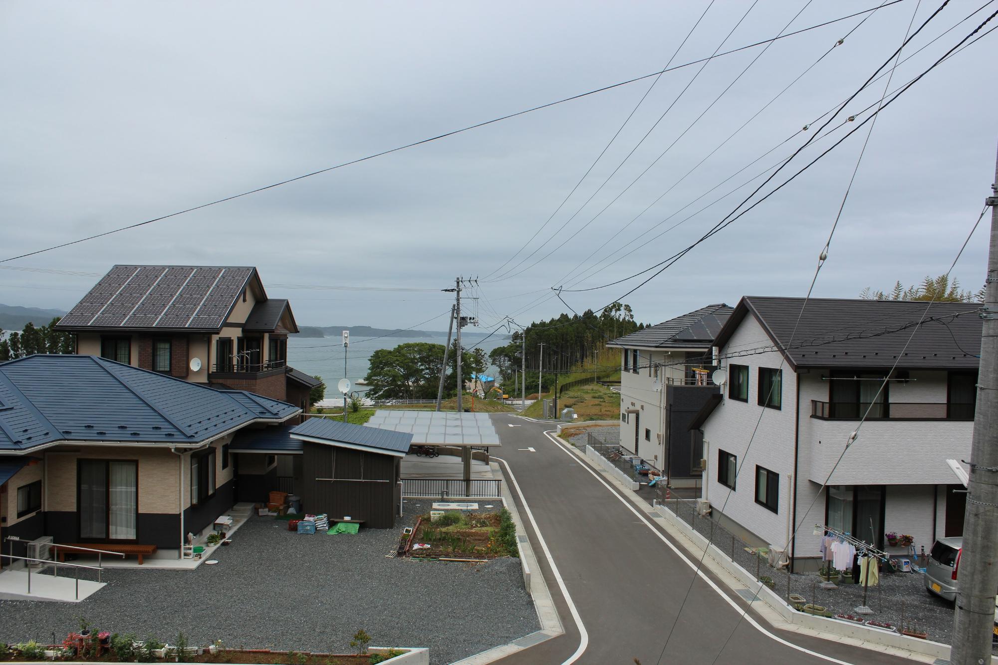 新しい住宅が立ち並ぶ整った街並みの奥に海が広がる風景の写真