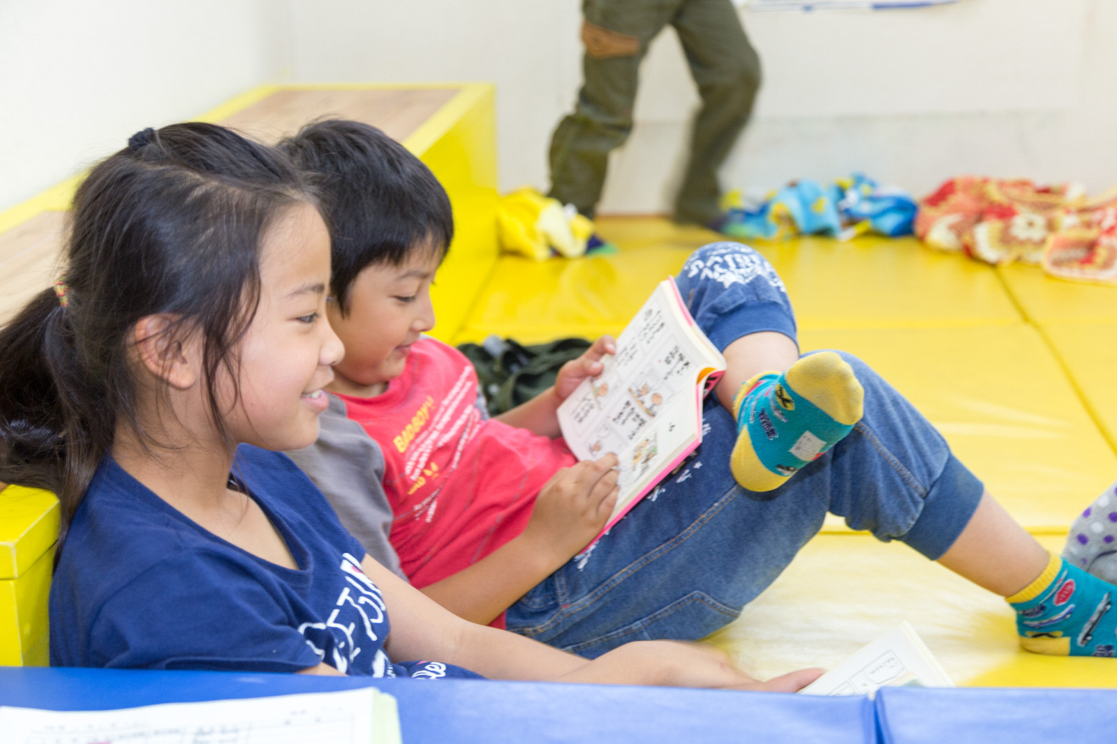 小学生の男女2人が黄色いマットの上に座りながらそれぞれ読書を楽しんでいる写真