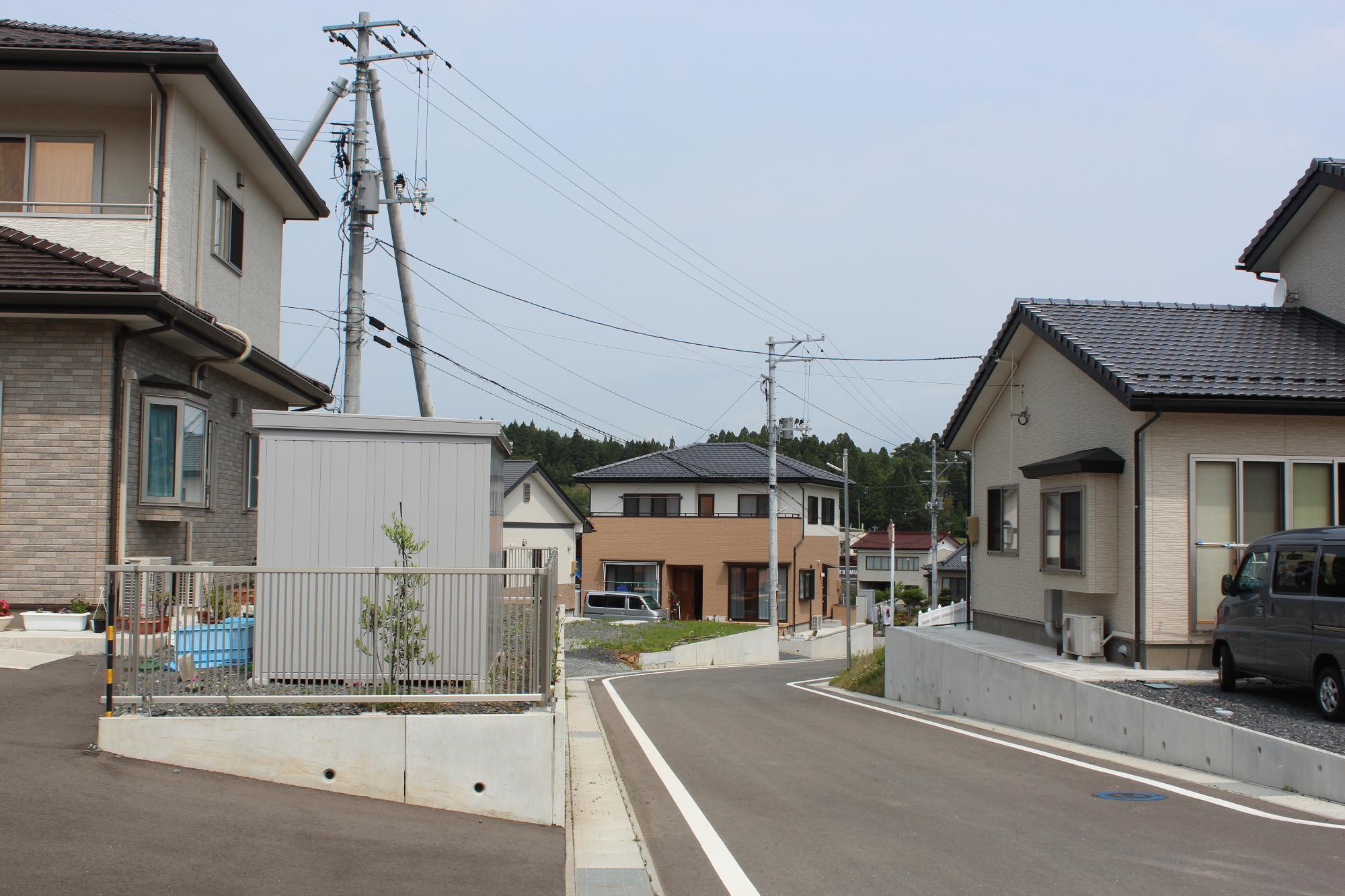 新しく整備された住宅地の中で複数の家が立ち並び、舗装された道路や電柱が見える住宅街の写真
